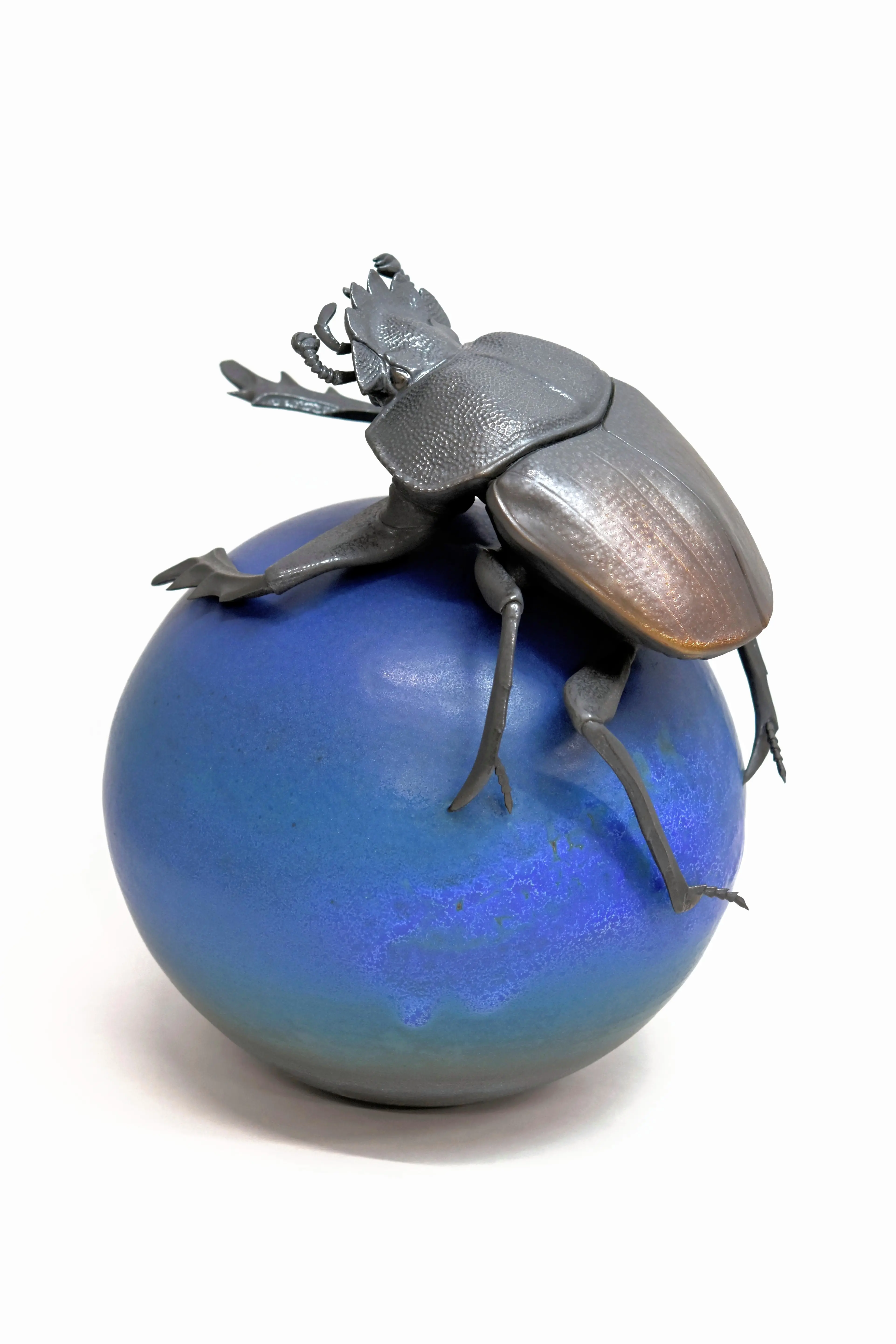 野村俊介の陶芸作品、一匹のスカラベが、鮮やかな青色の球体の上に載っている、スカラベは鈍く光る茶褐色をしている。