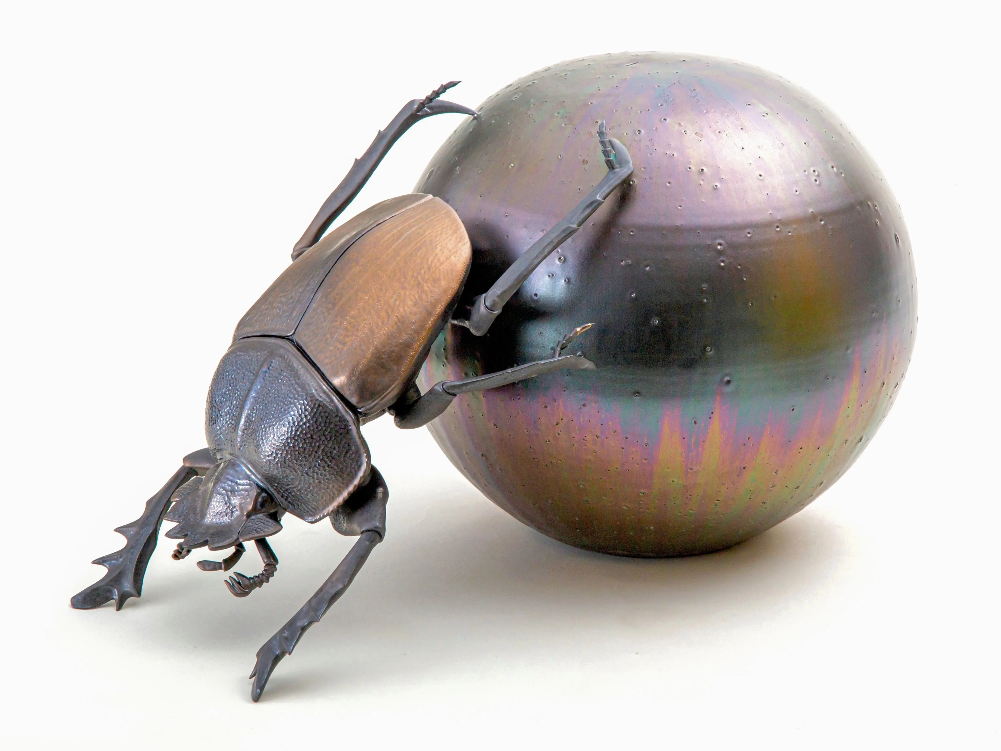 野村俊介の陶芸作品、一匹のスカラベが後ろ足で、金属光沢を有する褐色の球体を転がしている、スカラベは明るめの茶褐色をしており、鈍い光沢を放っている。